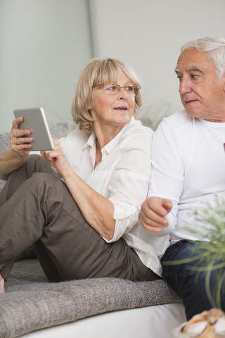 Älteres Paar mit digitalem Tablet nebeneinander auf dem Sofa im Wohnzimmer, lizenzfreies Stockfoto