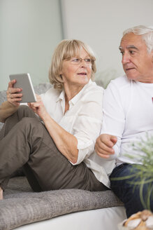 Älteres Paar mit digitalem Tablet nebeneinander auf dem Sofa im Wohnzimmer - WESTF019242