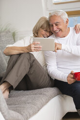 Älteres Paar mit digitalem Tablet nebeneinander auf dem Sofa im Wohnzimmer - WESTF019243