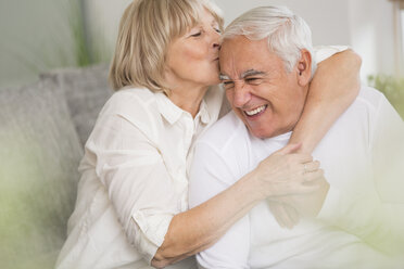 Senior woman kissing her husband in living room - WESTF019246