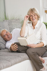 Älteres Paar mit Buch auf Sofa im Wohnzimmer - WESTF019250