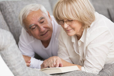Älteres Paar mit Buch nebeneinander auf dem Sofa liegend - WESTF019251