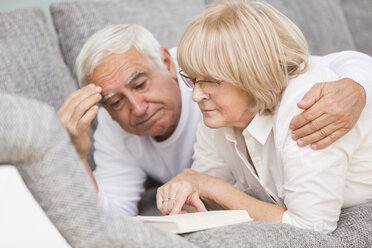 Älteres Paar mit Buch nebeneinander auf dem Sofa liegend - WESTF019252