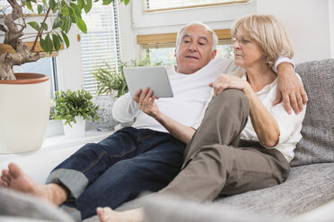 Senior couple with digital tablet side by side on sofa in living room - WESTF019257