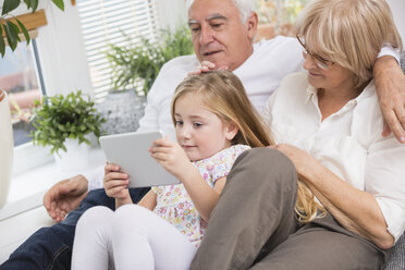Älteres Ehepaar und Enkelin sitzen mit digitalem Tablet auf dem Sofa im Wohnzimmer - WESTF019184