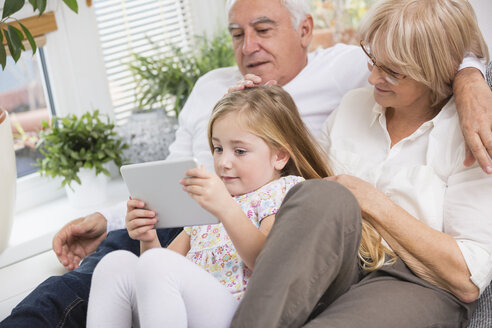 Älteres Ehepaar und Enkelin sitzen mit digitalem Tablet auf dem Sofa im Wohnzimmer - WESTF019184