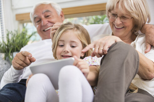 Älteres Ehepaar und Enkelin sitzen mit digitalem Tablet auf dem Sofa im Wohnzimmer - WESTF019182