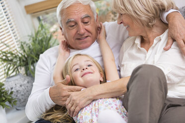 Senior couple and granddaughter relaxing on sofa in living room - WESTF019180