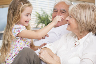 Senior couple and granddaughter relaxing on sofa in living room - WESTF019179