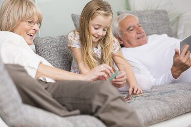 Ältere Frau und Enkelin spielen zusammen auf dem Sofa im Wohnzimmer - WESTF019172