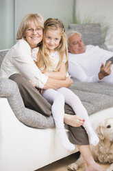 Porträt einer älteren Frau, die ihre Enkelin auf dem Sofa im Wohnzimmer umarmt - WESTF019171