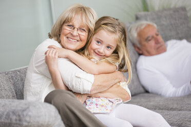 Porträt einer älteren Frau, die ihre Enkelin auf dem Sofa im Wohnzimmer umarmt - WESTF019169