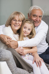 Portrait of senior couple with granddaughter on sofa in living room - WESTF019168