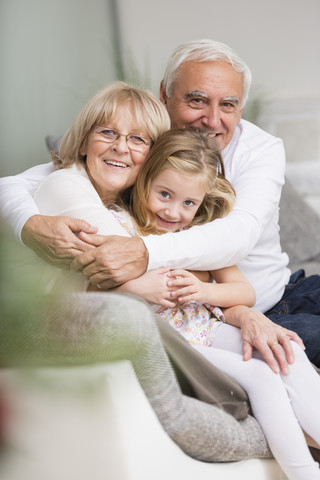 Porträt eines älteren Paares mit Enkelin auf dem Sofa im Wohnzimmer, lizenzfreies Stockfoto