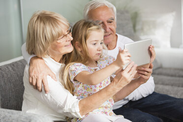 Senior couple and granddaughter looking at digital tablet at home - WESTF019164