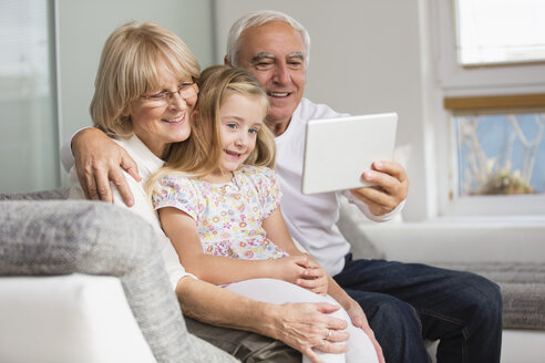 Älteres Ehepaar und Enkelin schauen sich zu Hause ein digitales Tablet an - WESTF019163