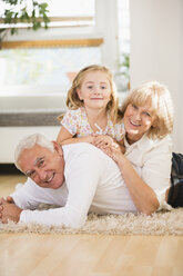 Family portrait of senior couple and granddaughter lying on the floor at home - WESTF019146