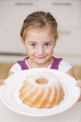 Porträt eines lächelnden kleinen Mädchens, das einen Teller mit Ringkuchen hält - WESTF019131