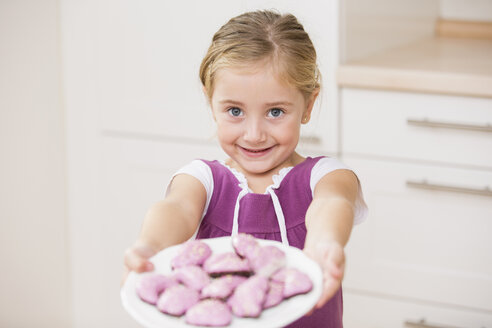 Porträt eines lächelnden kleinen Mädchens, das einen Teller mit rosa Keksen hält - WESTF019130