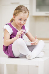 Porträt eines lächelnden kleinen Mädchens, das auf einem Tisch mit einem Teller mit rosa Keksen sitzt - WESTF019128