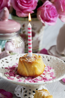 Muffin mit angezündeter Geburtstagskerze, Glas mit Marshmallows, Tasse und rosa Rosen auf dem Tisch - CSF021065