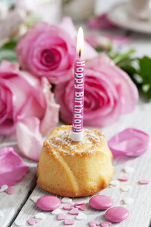 Muffin mit angezündeter Geburtstagskerze, Backdekor und rosa Rosen auf dem Tisch - CSF021068