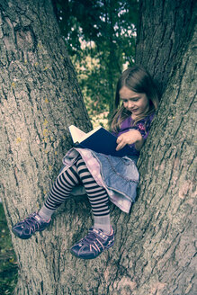 Kleines Mädchen sitzt auf einem Baumstamm und liest ein Buch - SARF000416