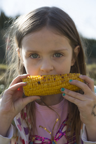 Porträt eines kleinen Mädchens, das gegrillte Maiskolben isst, lizenzfreies Stockfoto