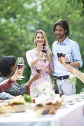 Couple holding glasses of red wine on a garden party - ABF000583