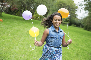 Smiling girl holding balloons in garden - ABF000575