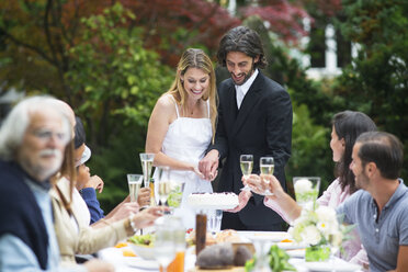 Braut und Bräutigam schneiden Hochzeitstorte auf einer Gartenparty an - ABF000601