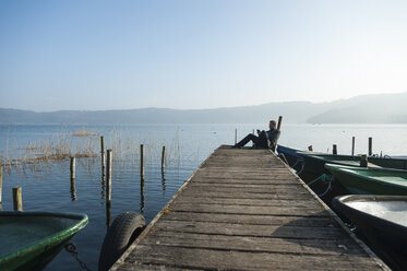 Man sitting on wooden boardwalk using tablet computer - PA000579