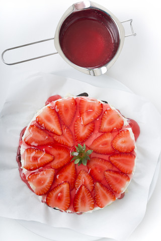 Topf mit rotem Tortenguss und Erdbeer-Frischkäse-Torte auf weißem Grund, Ansicht von oben, lizenzfreies Stockfoto