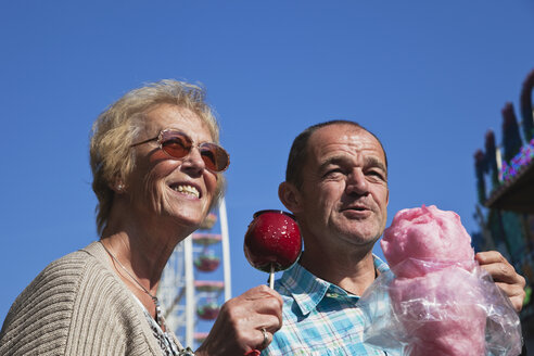 Mann und Frau auf dem Jahrmarkt genießen kandierte Äpfel und Zuckerwatte - GWF002696