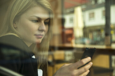 Deutschland, Mannheim, Junge Geschäftsfrau in einem Café, prüft ihr Mobiltelefon - UUF000014