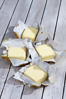 Vier Stücke Butter auf fettfreiem Papier und grauem Holztisch - CSF021146