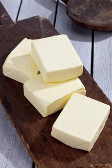 Vier Stücke Butter auf Holzbrett und grauem Holztisch - CSF021163