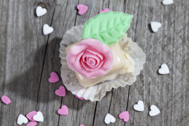 Petit four mit Rose aus Marzipan auf grauem Holz verziert - CSF021157