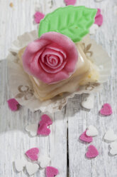 Petit four mit Rose aus Marzipan auf grauem Holz verziert - CSF021155