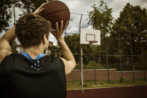 Junger Basketballspieler, der auf den Basketballkorb zielt, Rückansicht, lizenzfreies Stockfoto