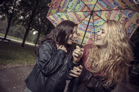 Zwei glückliche junge Frauen unter Regenschirm im Park, lizenzfreies Stockfoto