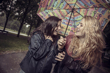 Zwei glückliche junge Frauen unter Regenschirm im Park - GCF000001
