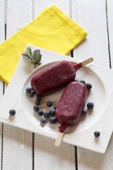 Teller mit zwei Wildbeeren-Eislutschern auf weißem Holztisch, Ansicht von oben - SARF000411