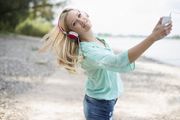 Junge Frau mit Kopfhörern tanzt am Strand - LFOF000157