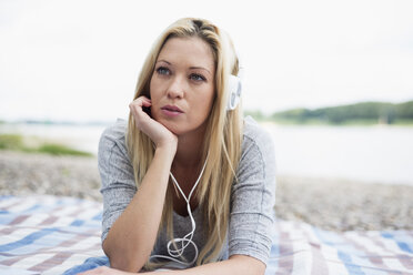Junge Frau mit Kopfhörern auf einer Decke am Strand liegend - LFOF000159