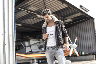Mann mit Lederjacke vor einem Propellerflugzeug in einem Hangar - MUMF000018