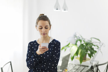 Young woman reading SMS on smartphone at home - EBSF000146