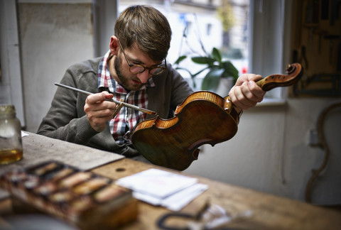 Violin maker in his workshop varnishing repaired violin stock photo