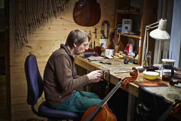 Geigenbauer in seiner Werkstatt beim Feilen einer Cellomechanik - DIKF000093