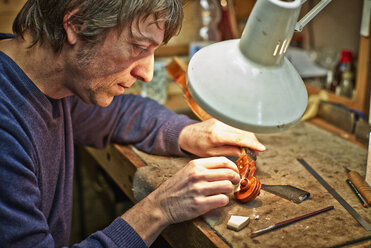 Geigenbauer in seiner Werkstatt bei der Reparatur einer Schnecke - DIKF000112